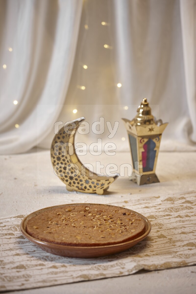 صحن من البسبوسة بجانب فوانيس علي خلفية بيضاء خشبية