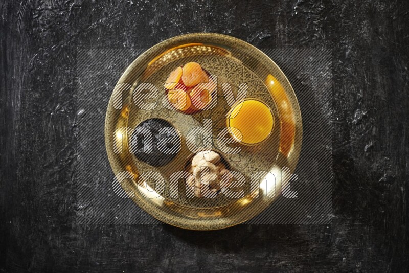 فواكه مجففة في أطباق معدنية مع مشروب قمر الدين على صينية علي خلفية سوداء