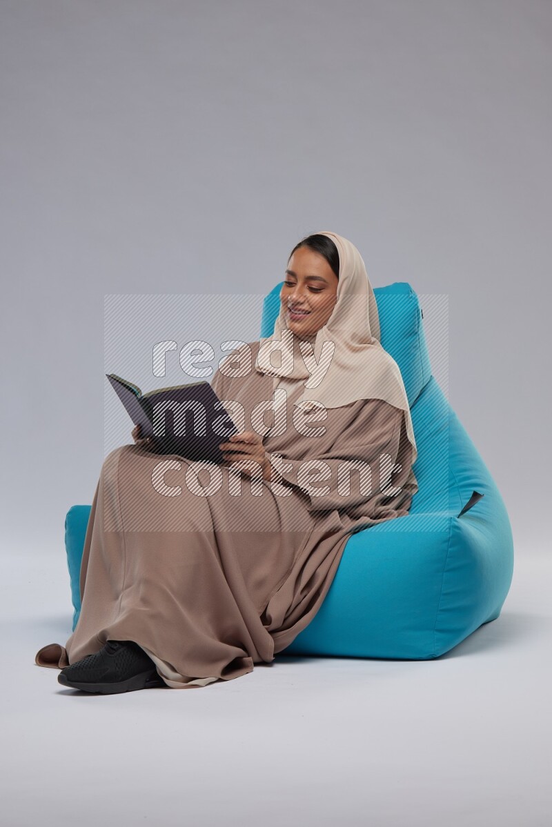 A woman sitting on a blue beanbag and reading a book
