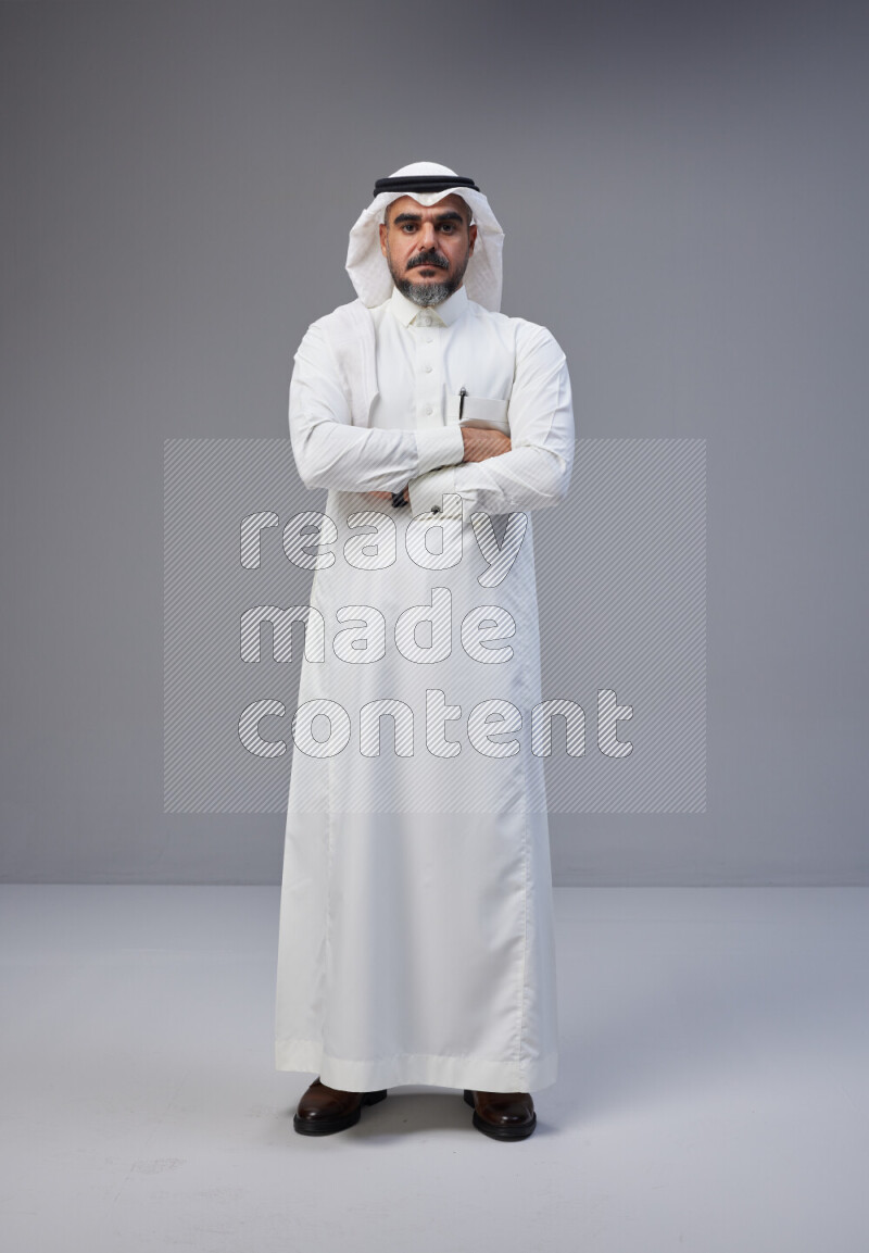 Saudi man Wearing Thob and white Shomag standing with crossed arms on Gray background