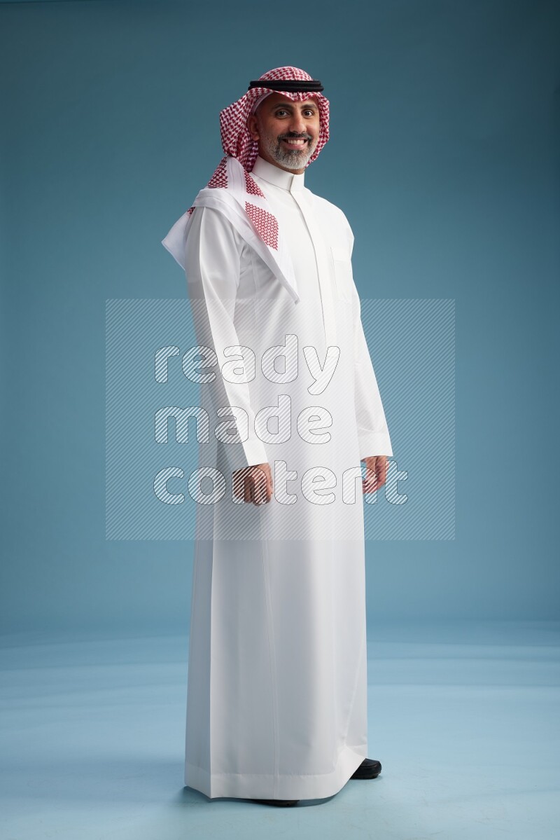 Saudi man wearing thob and shomagh posing to the camera on blue background