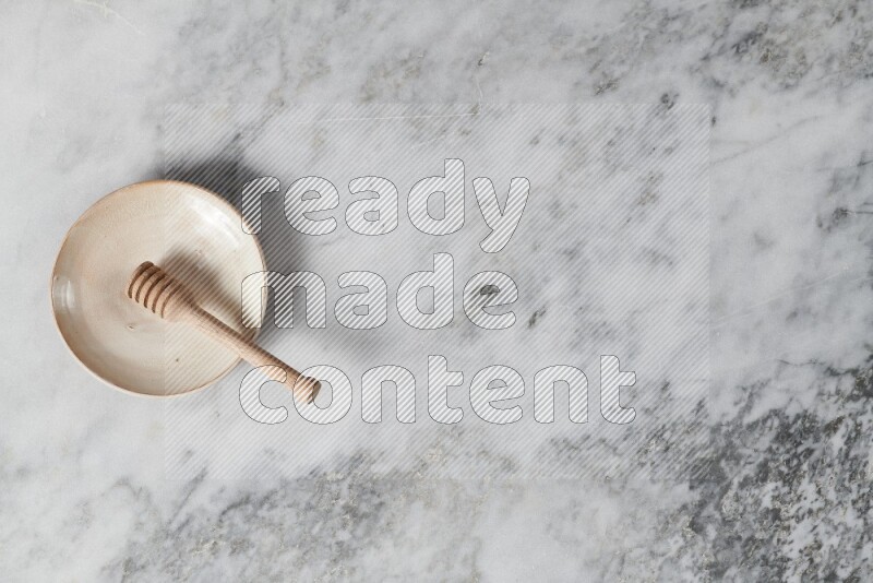 Beige pottery plate with wooden honey dipper in it on grey marble background