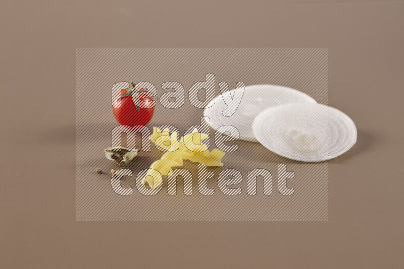 Raw pasta with different ingredients such as cherry tomatoes, garlic, onions, red chilis, black pepper, white pepper, bay laurel leaves, rosemary and cardamom on beige background