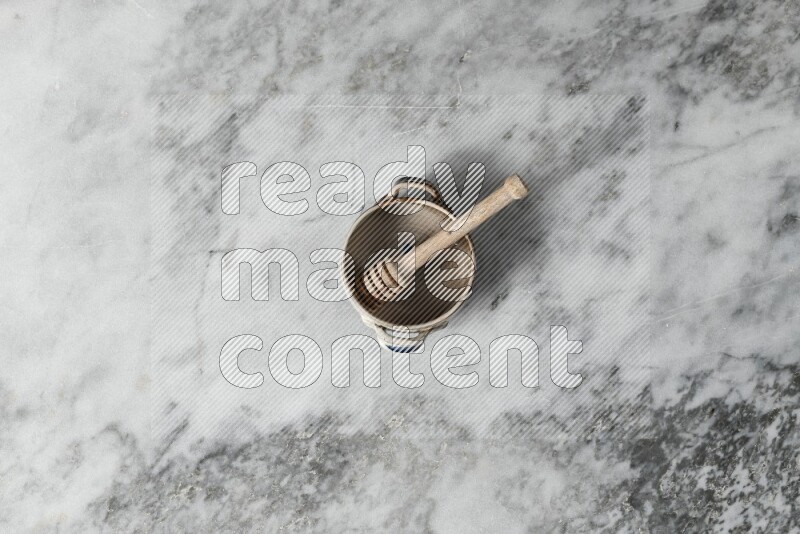 Multicolored pottery bowl with wooden honey dipper in it on grey marble background