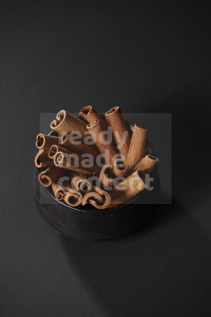 Cinnamon sticks in a black bowl on a black background in different angles