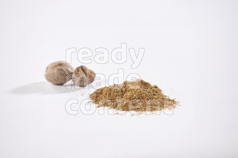 Nutmeg whole seeds with nutmeg powder beside it on a white flooring