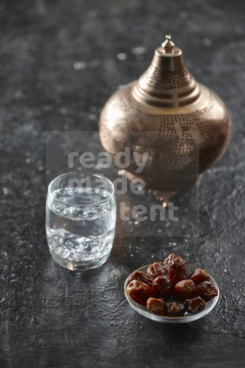 A golden lantern with different drinks, dates, nuts, prayer beads and quran on textured black background