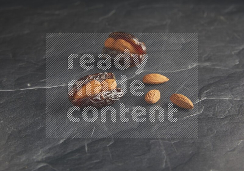 two almond stuffed madjoul dates on a black textured background