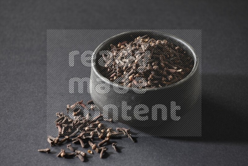 A black pottery bowl full of cloves on a black flooring