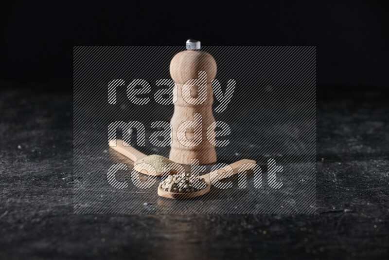 ملعقتان خشبيتان، واحدة ممتلئة ببودرة الفلفل الأبيض والأخرى بحبوب الفلفل ومطحنة خشبية على أرضية سوداء