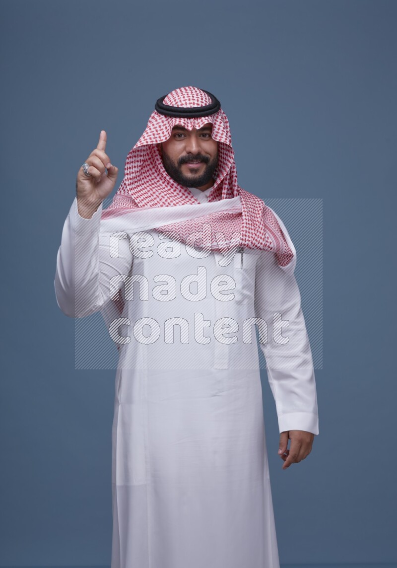 A Saudi man posing on blue background wearing Thob and Shomag