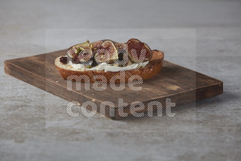 figs halves with cream cheese on toasted sourdough slice on a wooden board on textured grey background