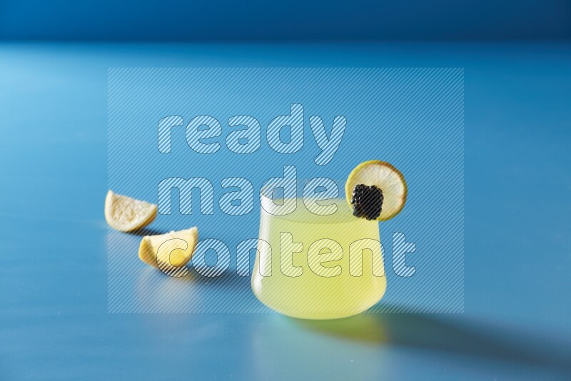 glass of lemon juice with lemon slice and berry on blue background