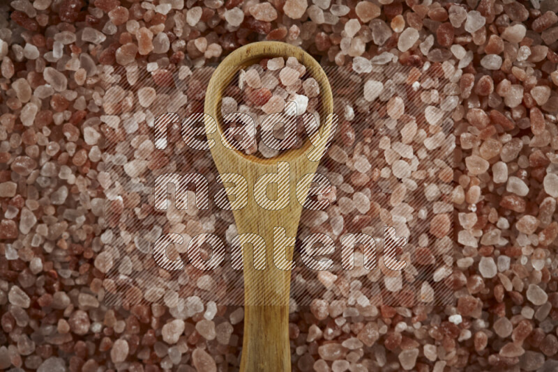 A wooden spoon full of coarse himalayan salt crystals on a bunch of the crystals on black background