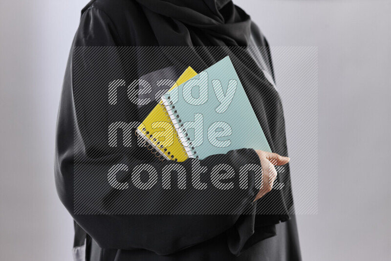 A woman in abaya holding books and a board in different positions (back to school)