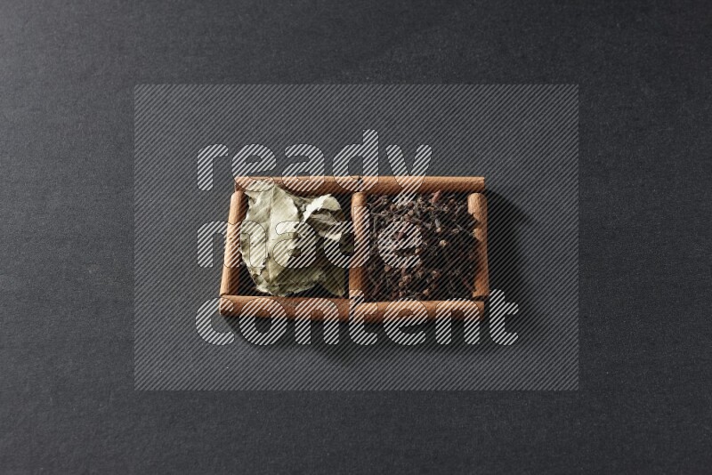 مربعان من أعواد القرفة ممتلئان بالقرنفل وأوراق الغار علي خلفية سوداء