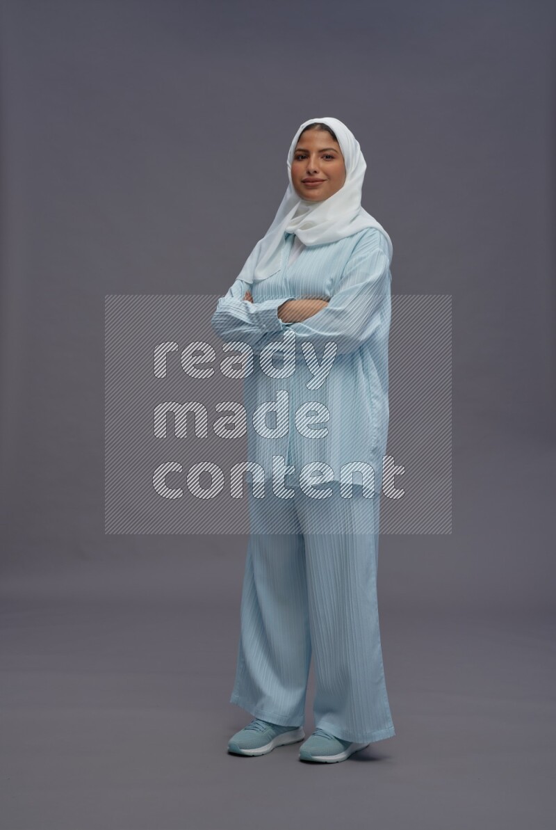 Saudi woman wearing hijab clothes standing with crossed arms on gray background
