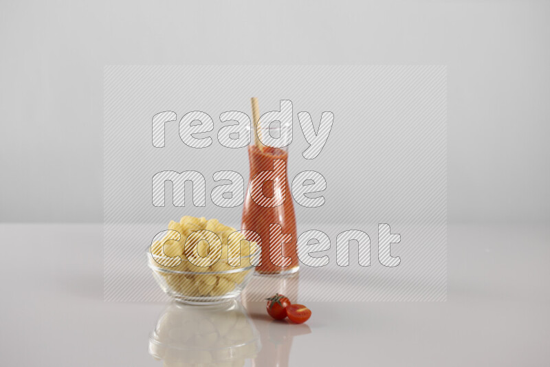 Raw pasta with tomatoe pasta with different ingredients such as cherry tomatoes, basil, garlic, bay laurel, cardamom, white pepper, black pepper, red chilis and wheat stalks on light grey background