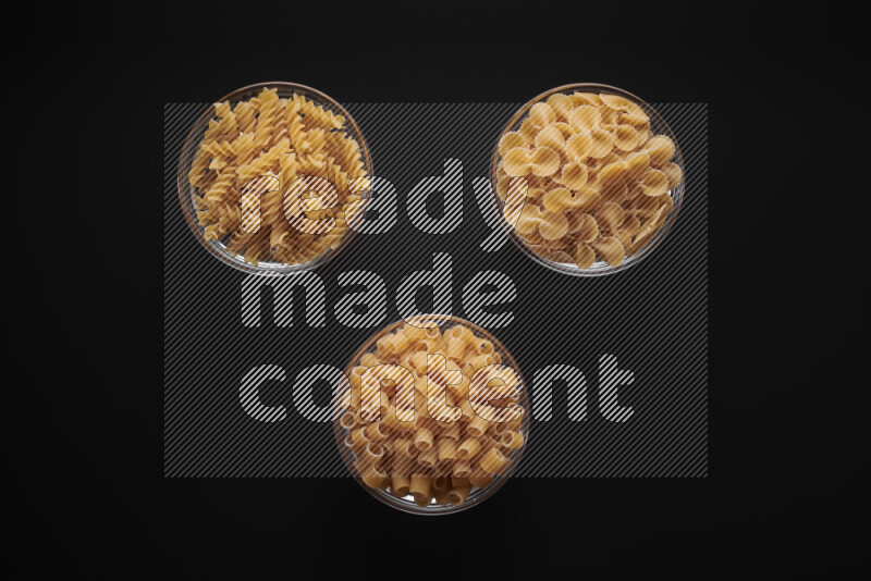 Different pasta types in glass bowls on black background