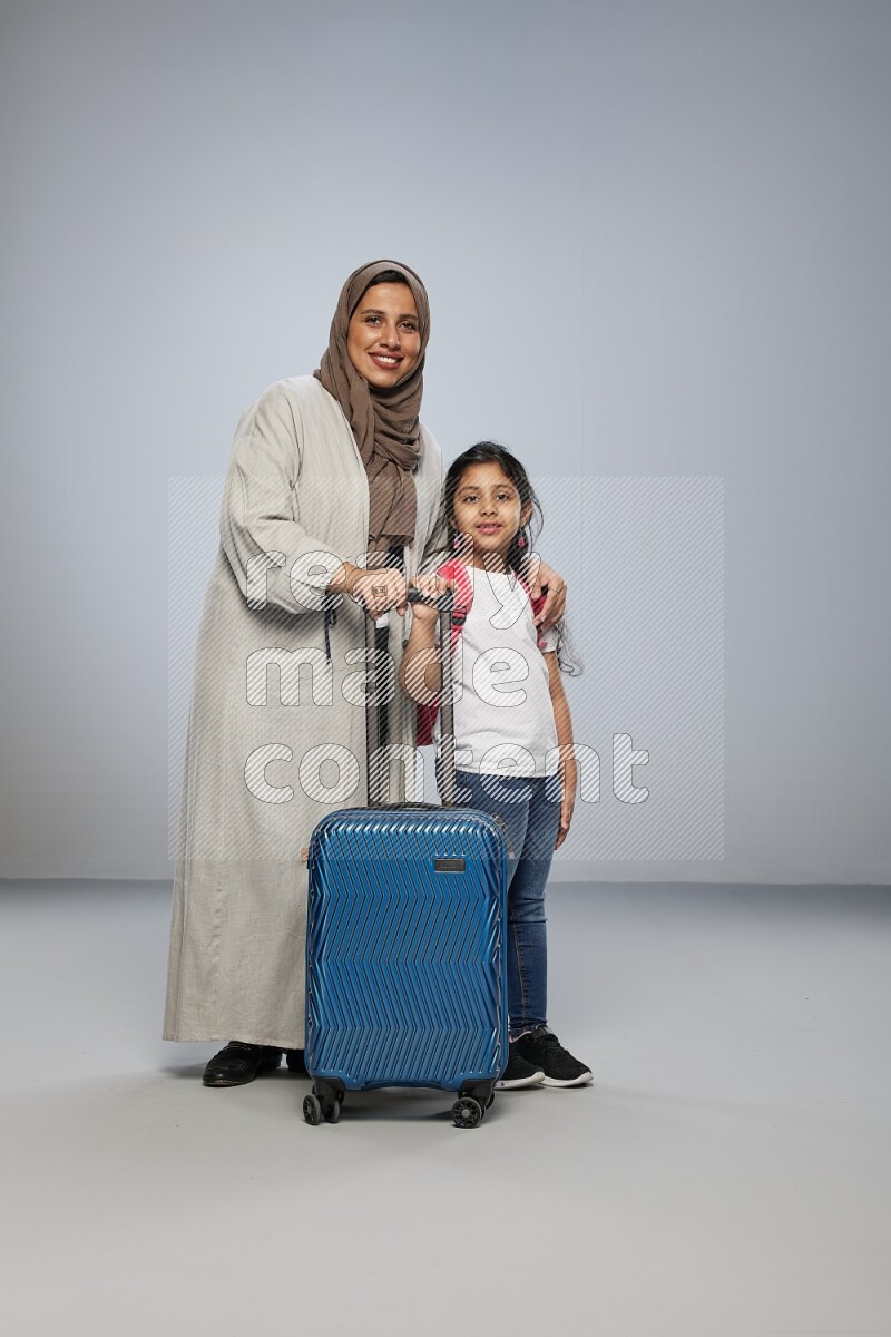 Mom and daughter standing pulling a carry-on bag on gray background