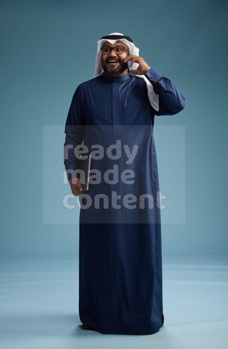 Saudi Man with shimag Standing talking on phone on blue background