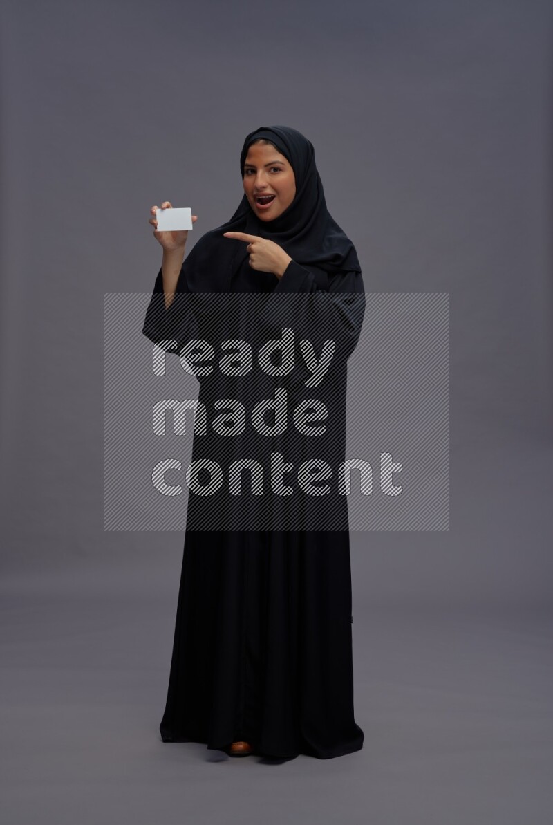 Saudi woman wearing Abaya standing holding ATM card on gray background