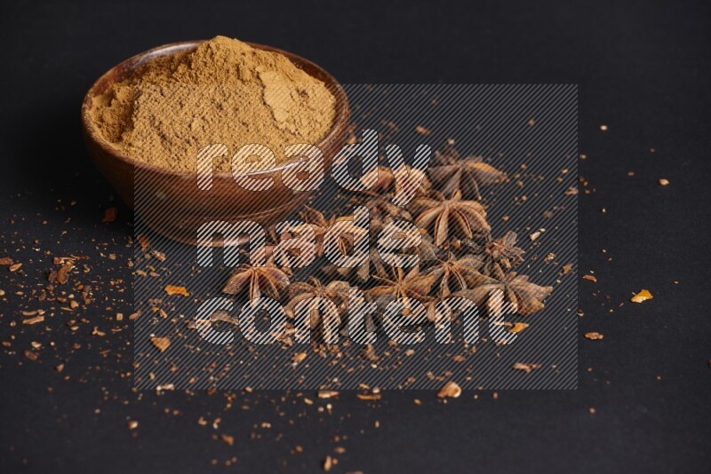 Star Anise powder in a wooden bowl with star anise beside it on a black background