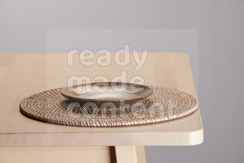 multi-colored pottery Plate placed on a big light colored straw placemat on the edge of wooden table