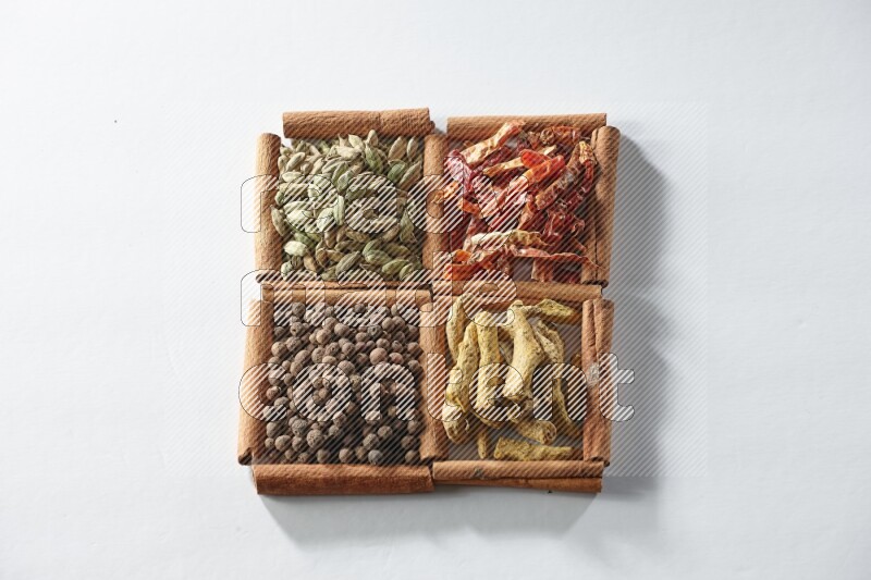 4 مربعات من أعواد القرفة ممتلئة بالفلفل الأحمر المجفف والهيل وأصابع الكركم وبهار الفلفل الحلو على أرضية بيضاء