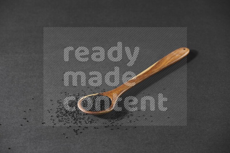 A wooden ladle full of black seeds and the seeds spread beside it on a black flooring