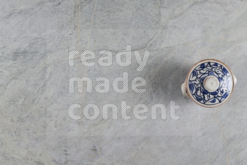 A multicolored pottery pot with its lid on grey marble background