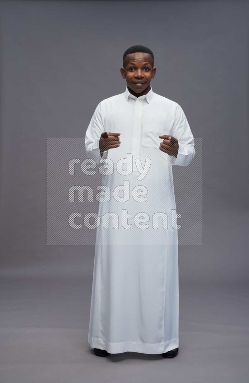 Saudi man wearing thob standing interacting with the camera on gray background
