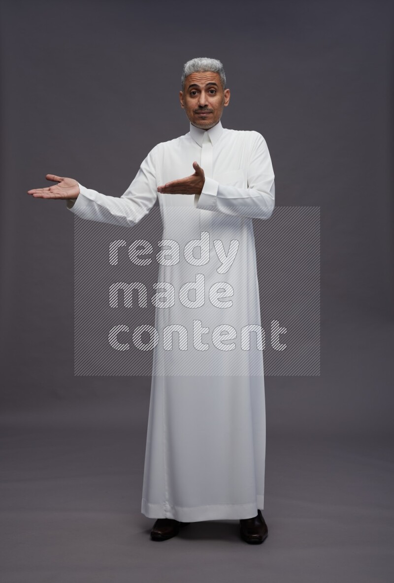 Saudi man wearing thob standing interacting with the camera on gray background