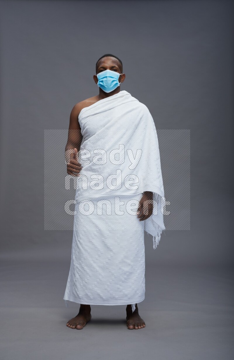 A man wearing Ehram with face mask Standing Interacting with the camera on gray background