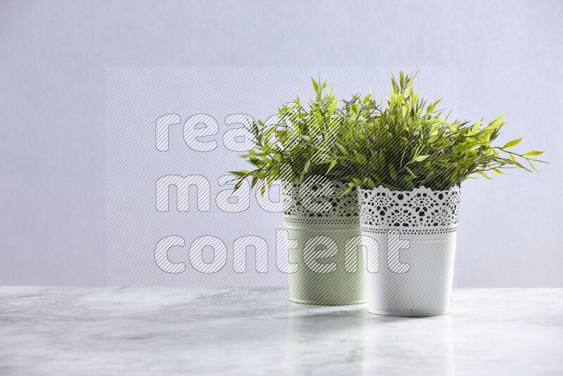 Two different artificial plants in white and green decorative pots on grey marble background