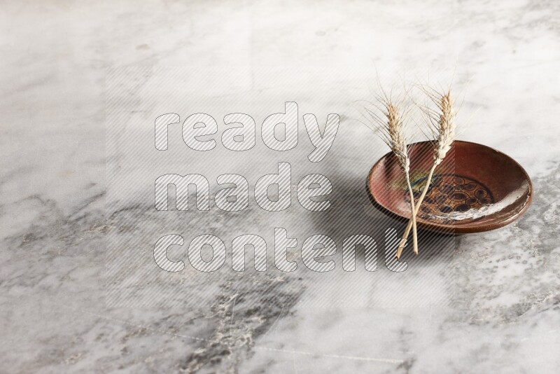 Wheat stalks on decorative pottery plate on grey marble background