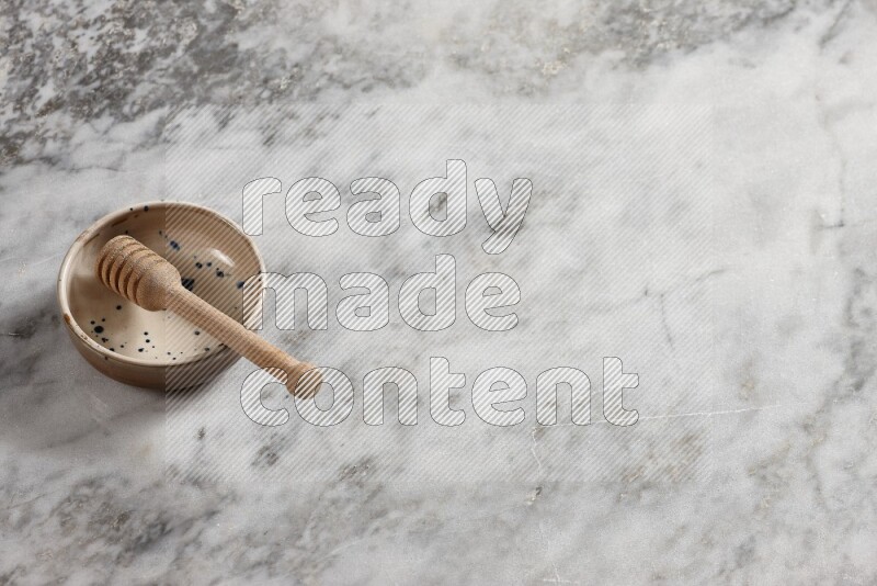 Multicolored pottery bowl with wooden honey dipper in it on grey marble background