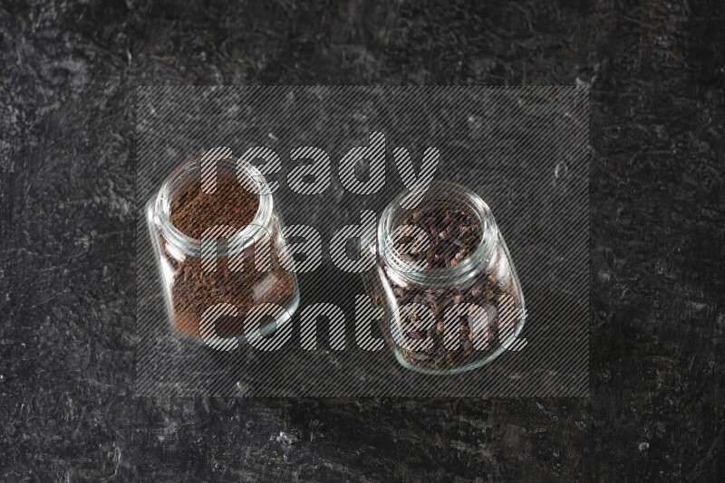 Glass spice jars full of cloves and cloves powder on textured black flooring