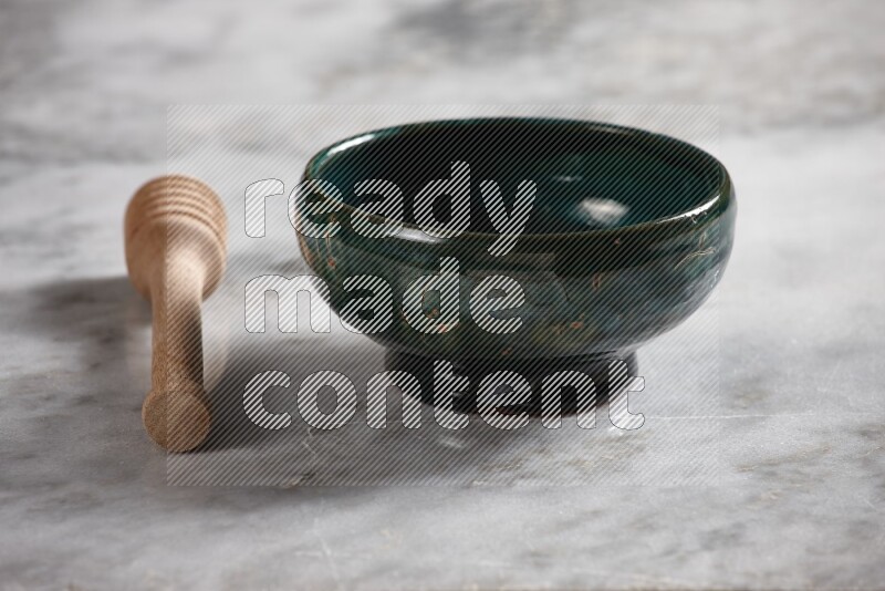 Dark green pottery bowl with wooden honey dipper on the side on grey marble background