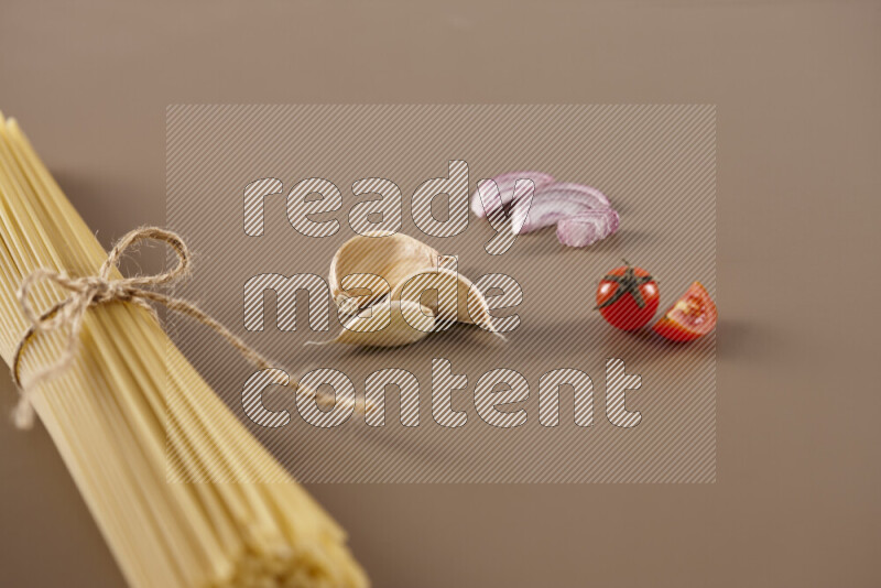 Raw pasta with different ingredients such as cherry tomatoes, garlic, onions, red chilis, black pepper, white pepper, bay laurel leaves, rosemary and cardamom on beige background
