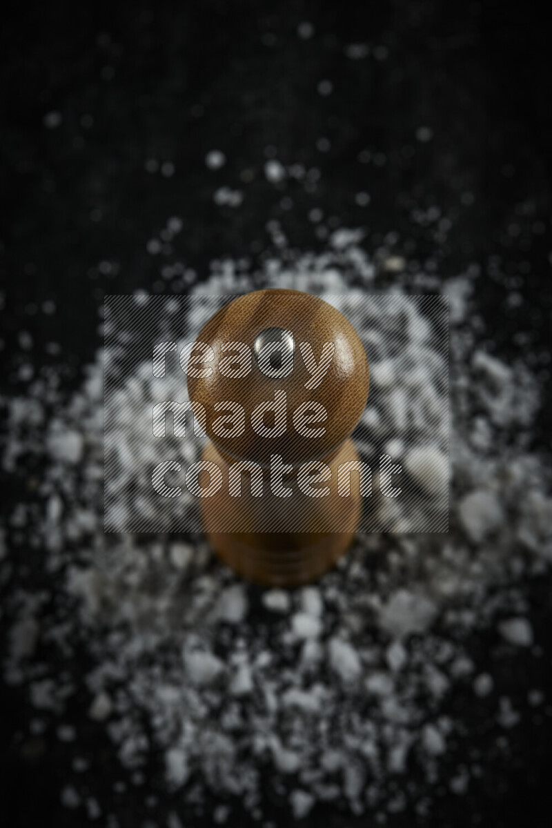 A wooden grinder standing upright and surrounded by coarse white sea salt on black background