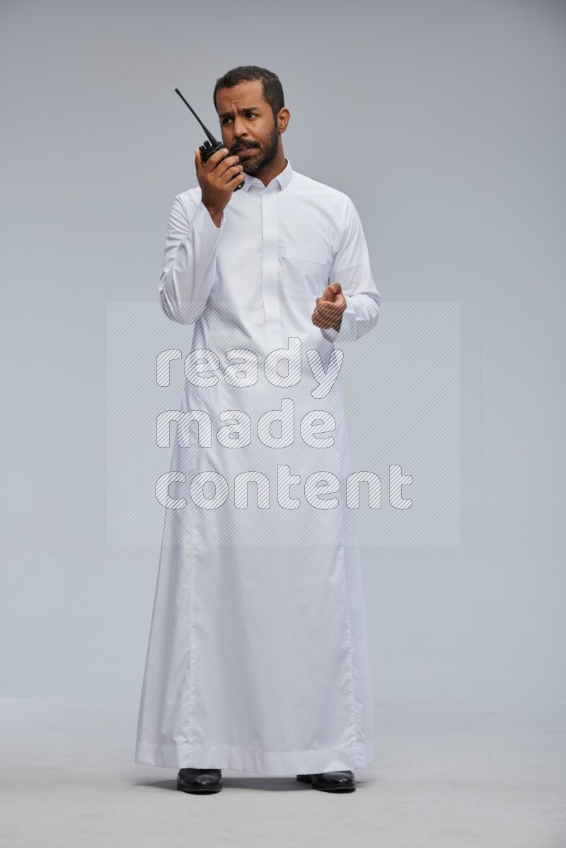 Saudi man Wearing thob standing holding walkie-talkie on Gray background