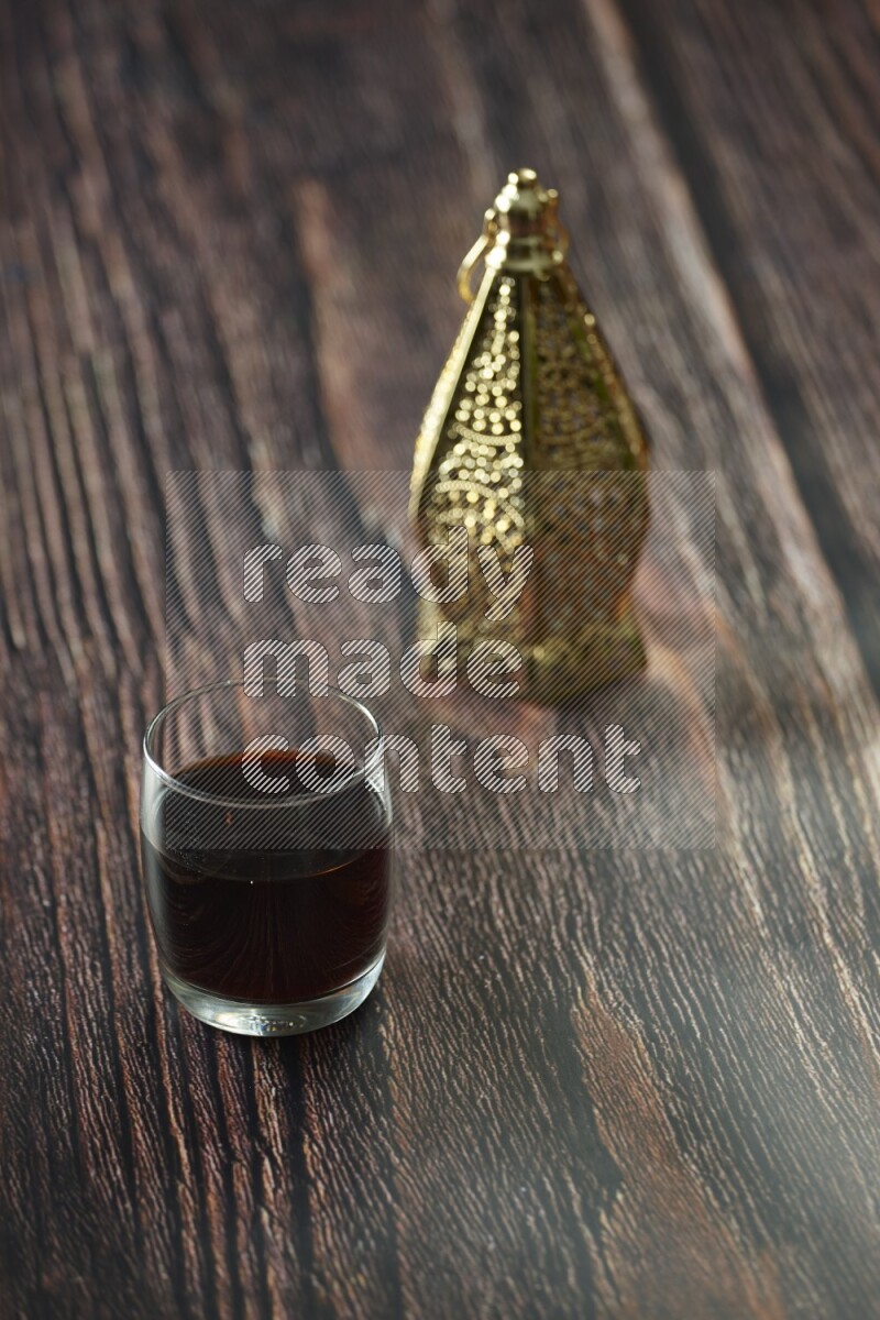 A golden lantern with different drinks, dates, nuts, prayer beads and quran on brown wooden background