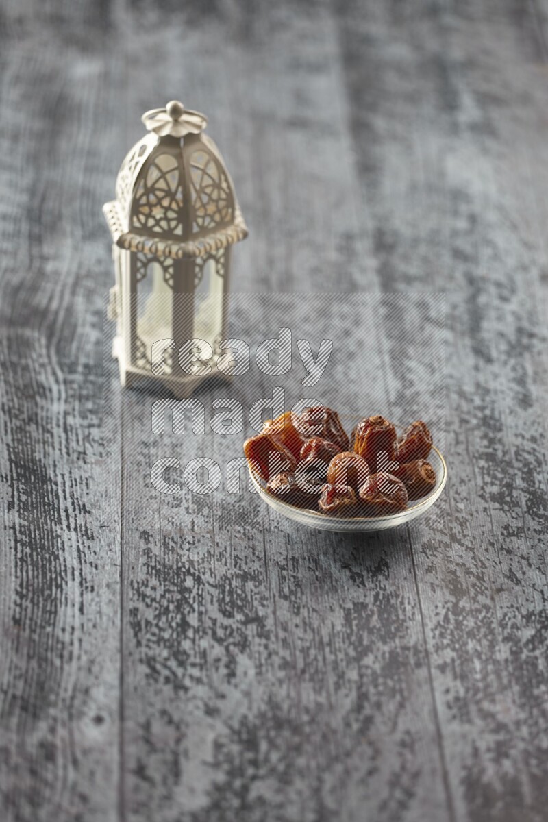 A white lantern with different drinks, dates, nuts, prayer beads and quran on grey wooden background