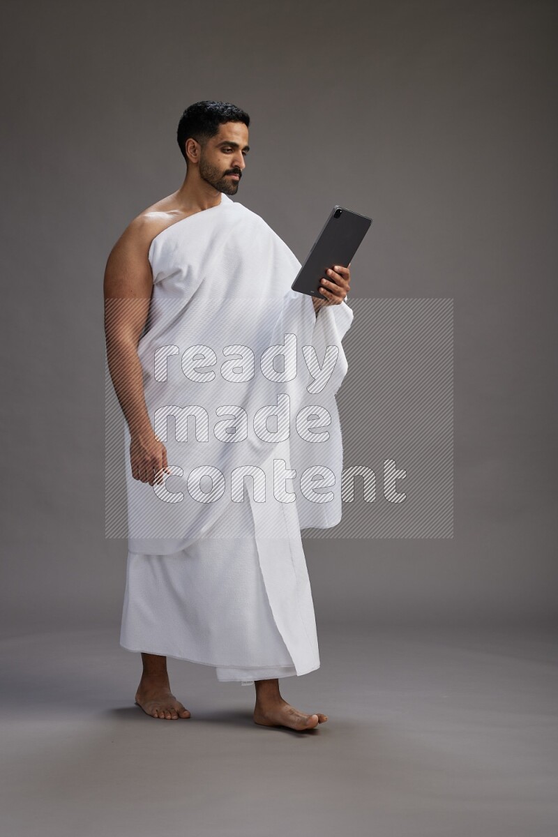 A man wearing Ehram and holding a tablet on gray background
