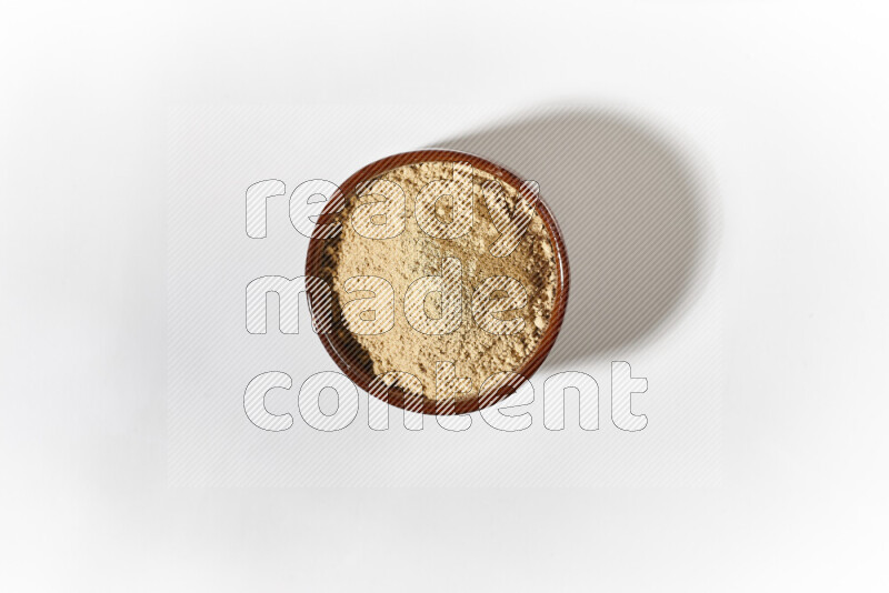 A brown pottery bowl full of ground ginger powder on white background