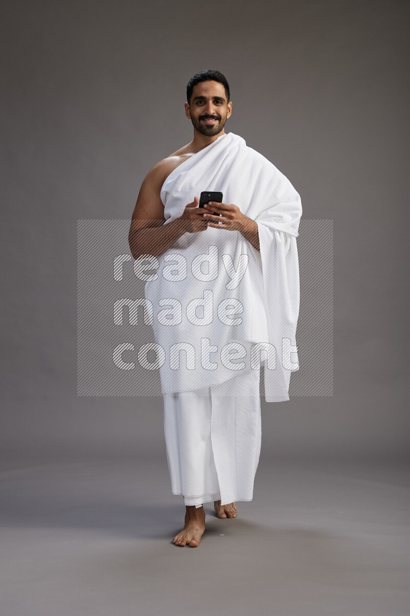 A man wearing Ehram Standing texting on phone on gray background