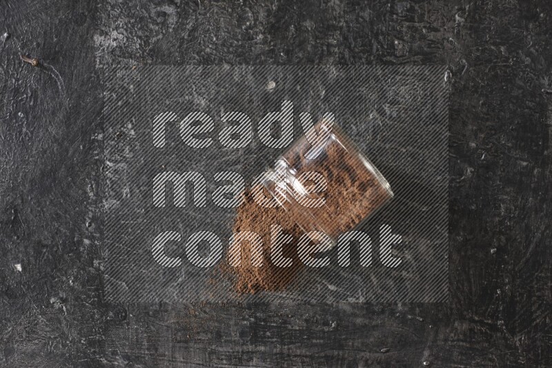 A flipped glass jar full of cloves powder on a textured black flooring