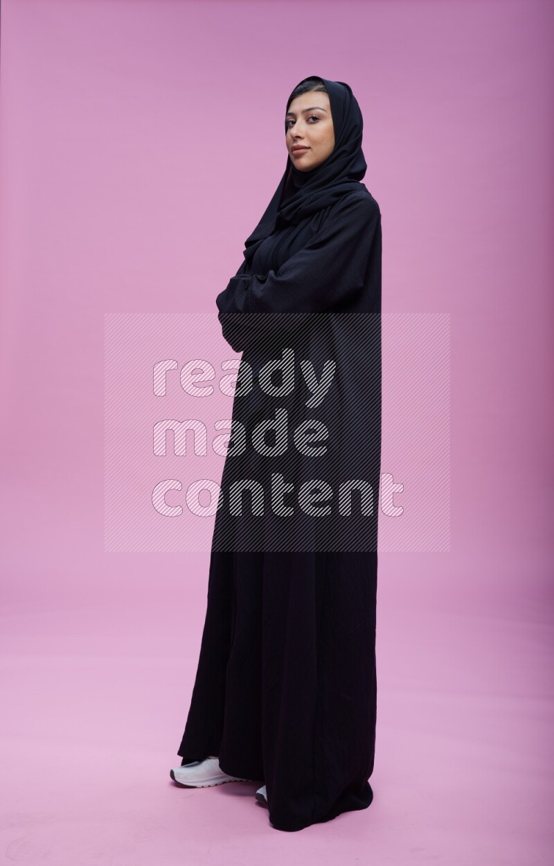 Saudi woman wearing Abaya standing with crossed arms on pink background