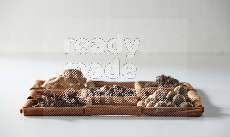 9 مربعات من أعواد القرفة ممتلئة بحبوب القهوة في المنتصف محاطة بالنعناع المجفف والزنجبيل المجفف وحبوب الهيل واليانسون النجمي والقرفة وجوزة الطيب والريحان المجفف والقرنفل على أرضية بيضاء